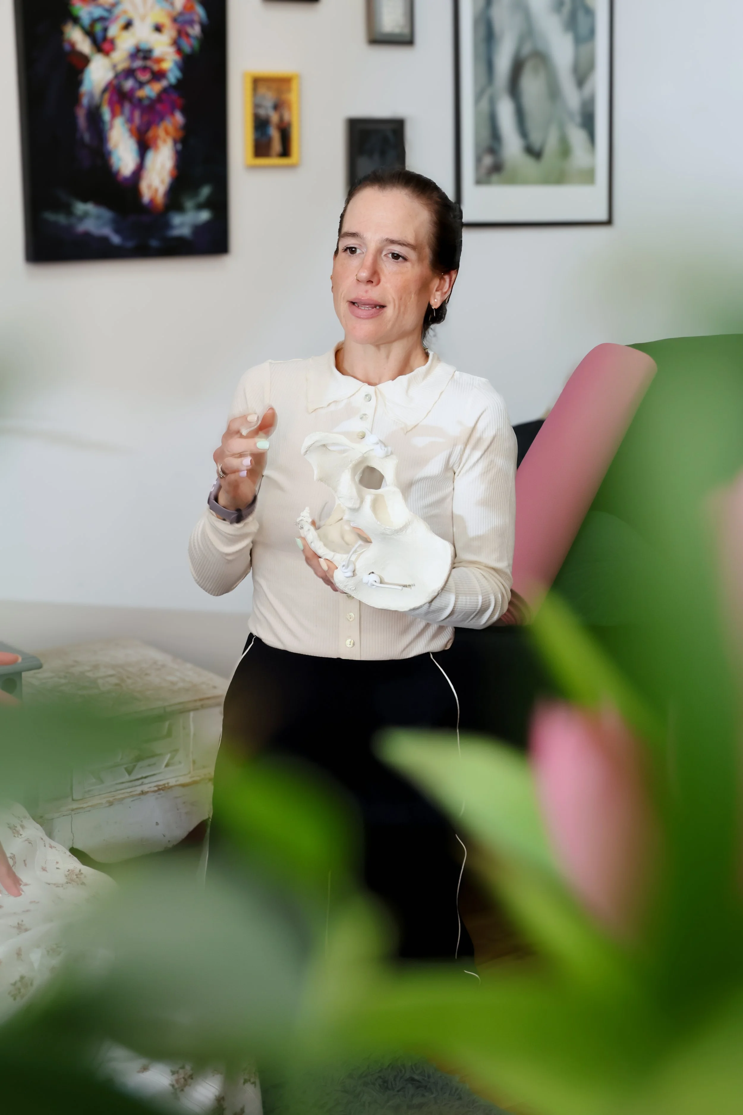 A woman holding a skull model in a room with framed artwork on the wall.