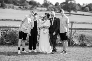 Four men and a woman stand together outdoors near a grassy field and a fence, smiling and celebrating.
