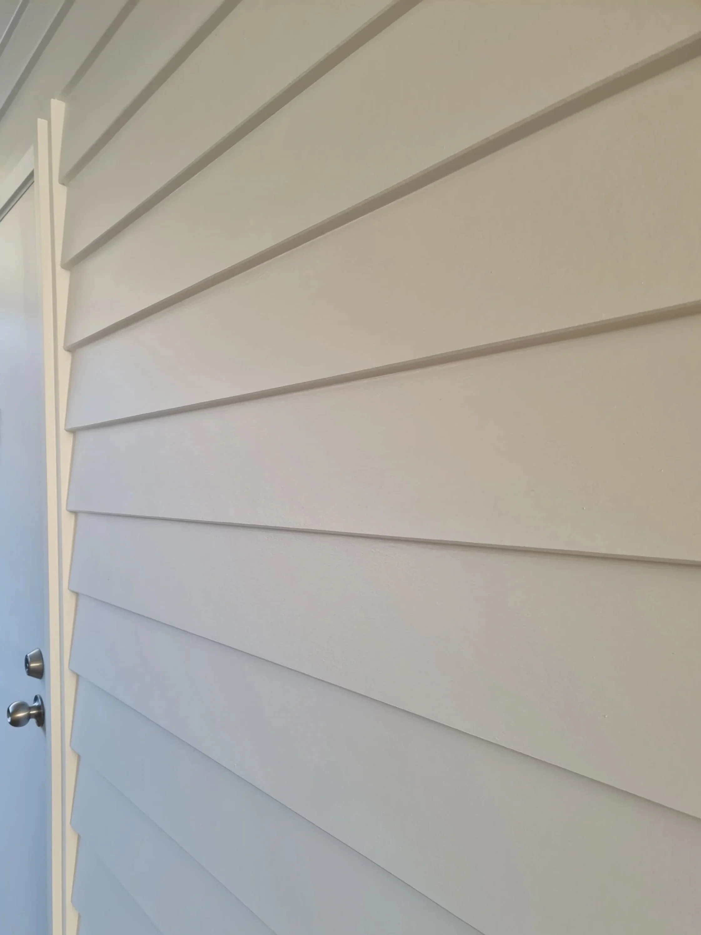 Close-up of white horizontal weatherboard cladding on building exterior with a partially visible door and door handle.