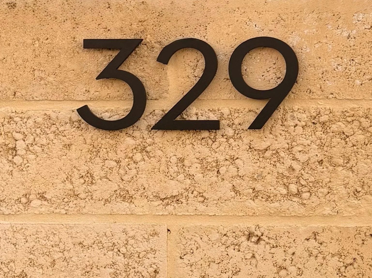 House number 329 mounted on a textured limestone wall.
