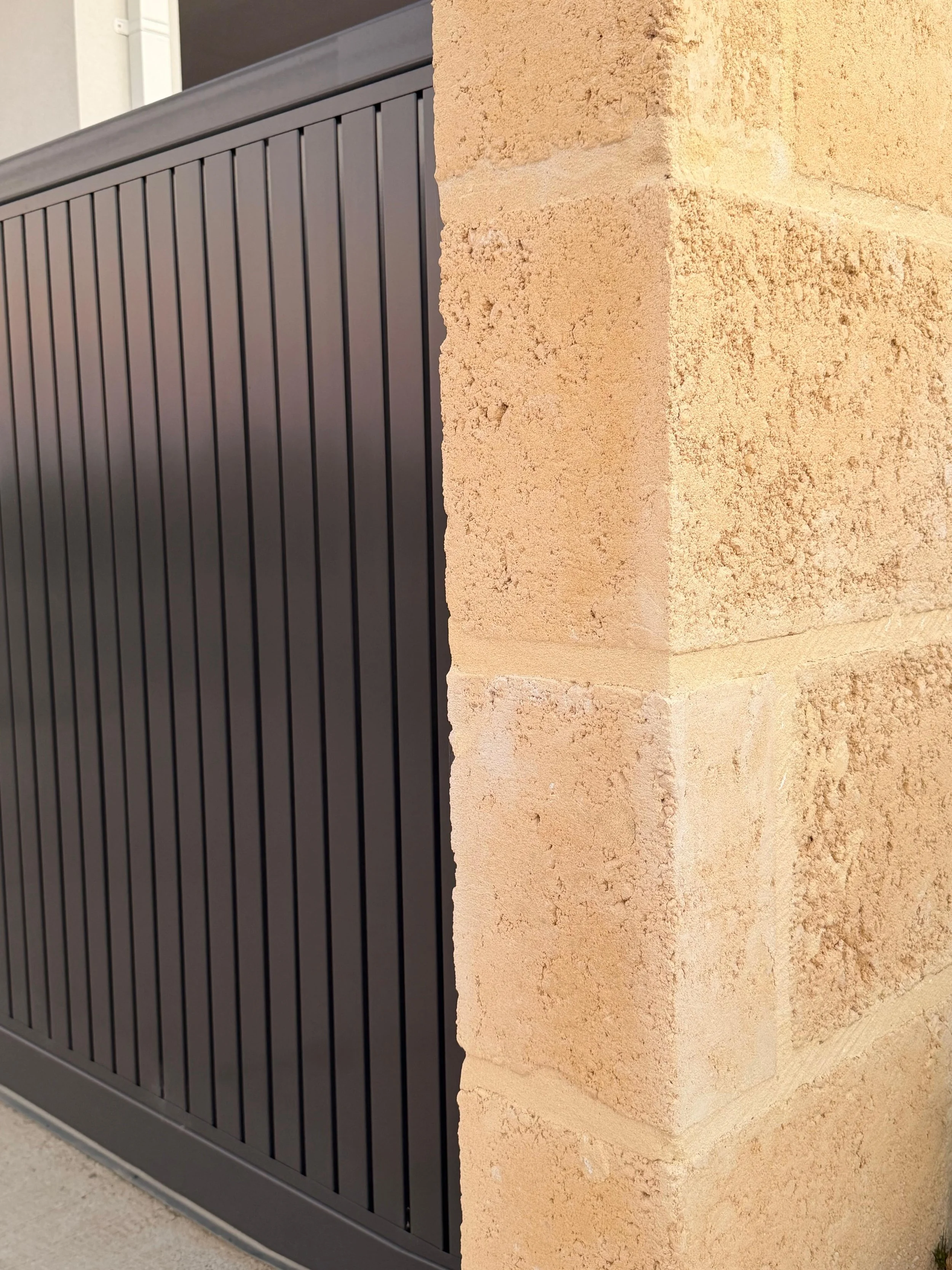 A black metal gate with vertical bars adjacent to a limestone brick wall.