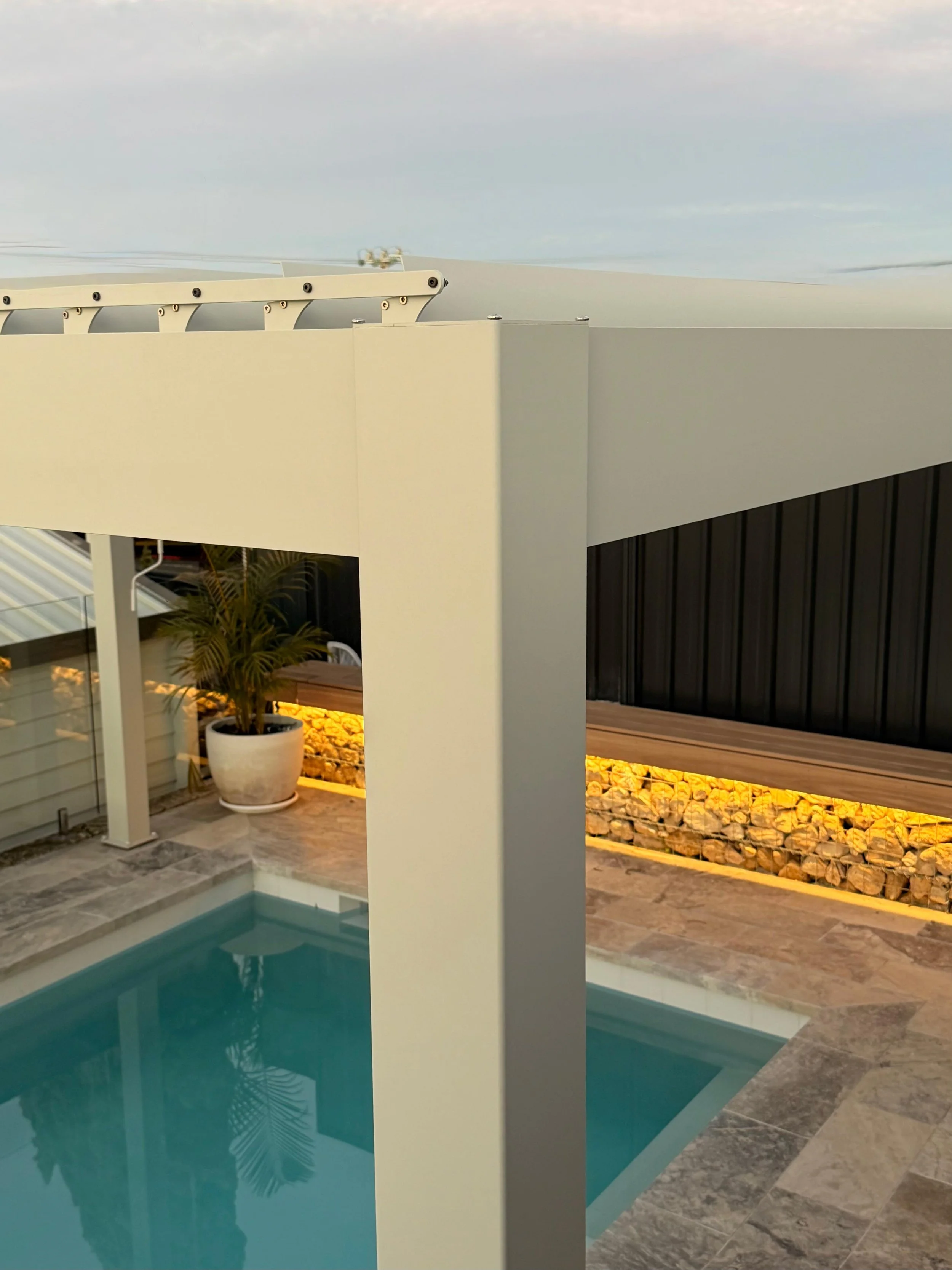 Modern residential outdoor area featuring a swimming pool, potted plant, and a decorative wall with lighting, rocks, and a partial view of a balcony or patio.
