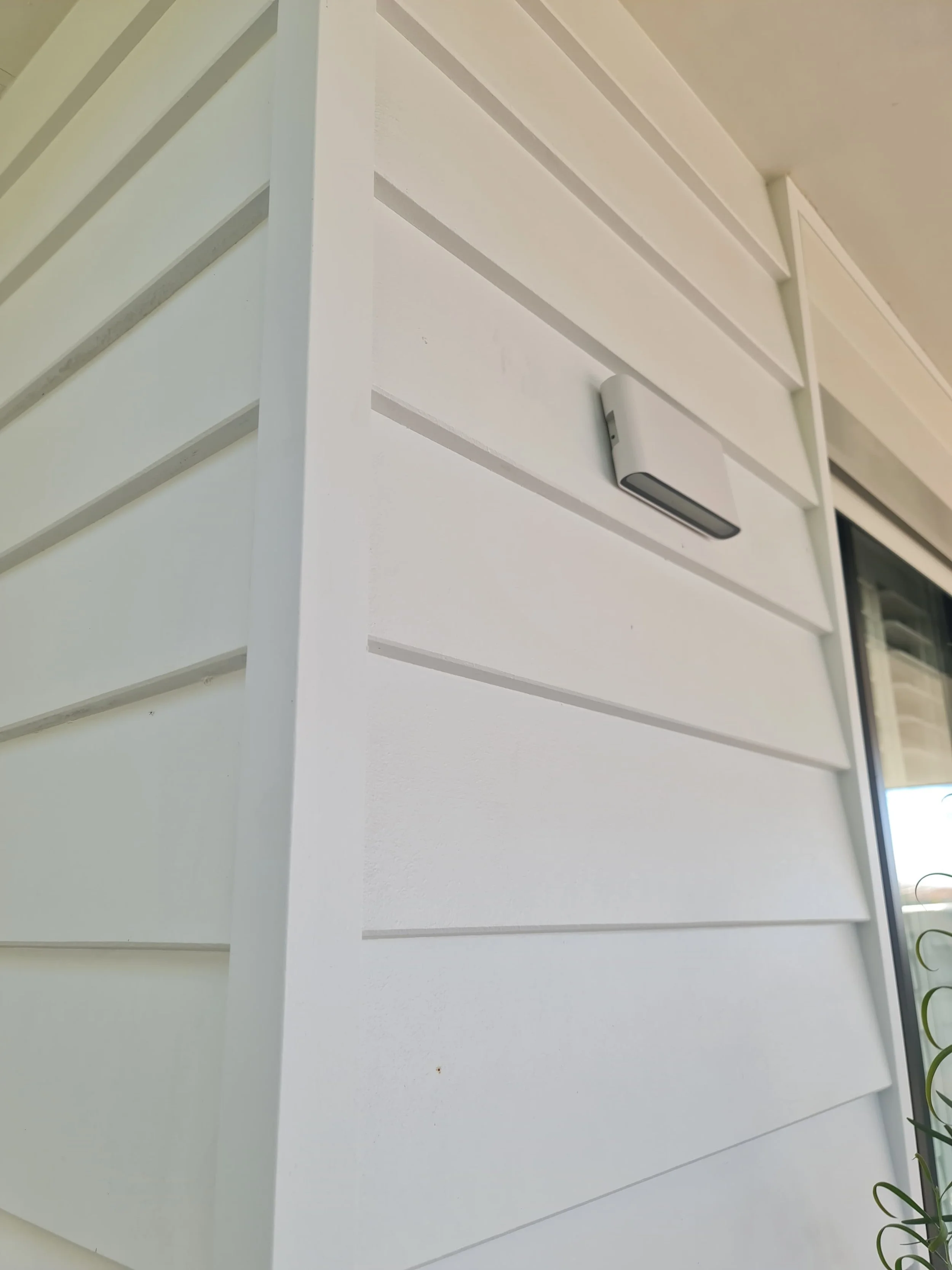 Close-up of white weatherboard cladding with a small white outdoor light fixture mounted on the wall.