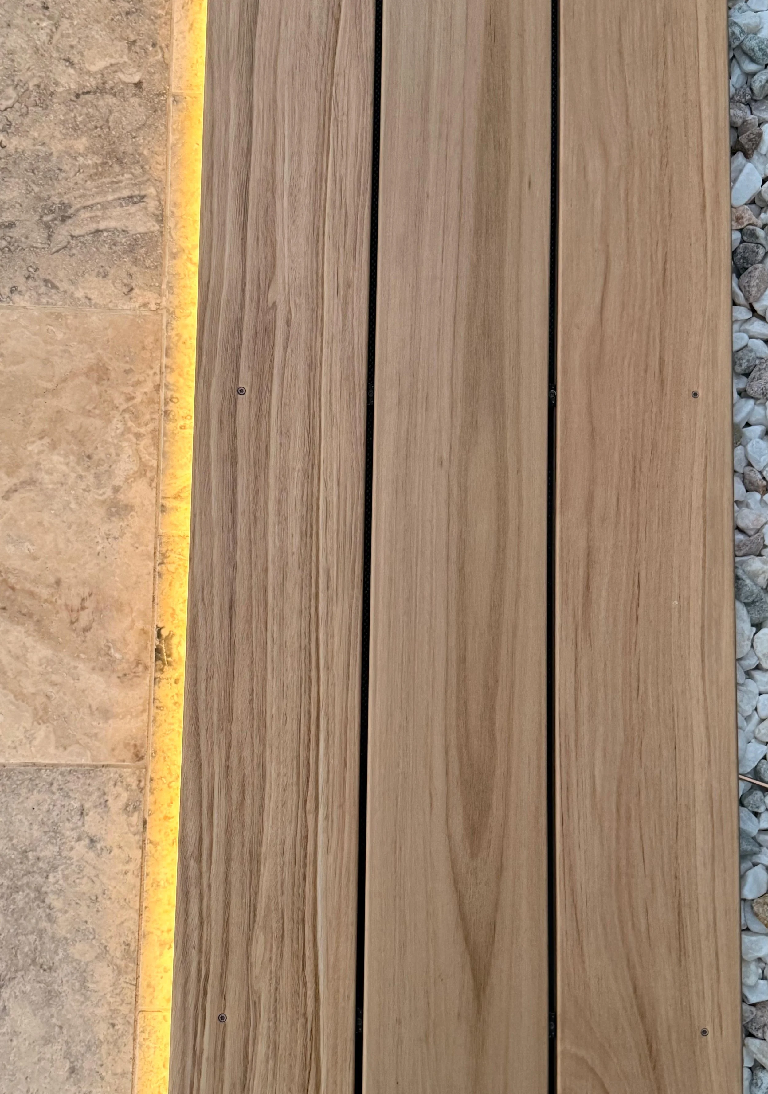 Close-up of a wooden bench seat, surrounded by gravel and travertine paving