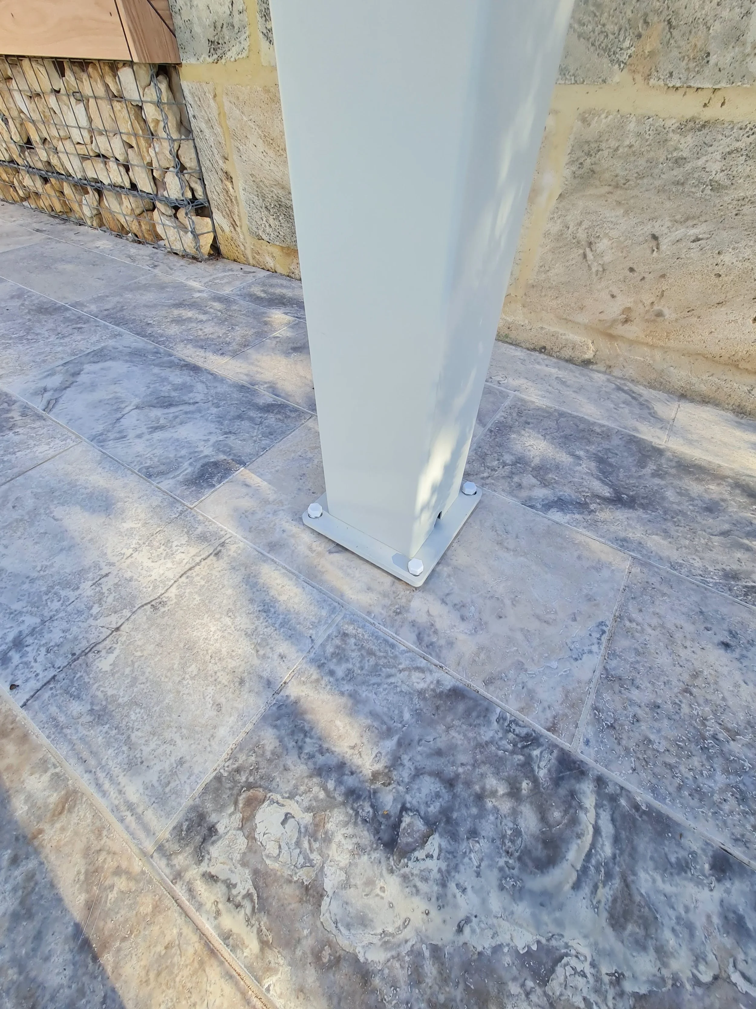 A close-up photo of a bioclimatic pergola column showing drainage hole and fixings