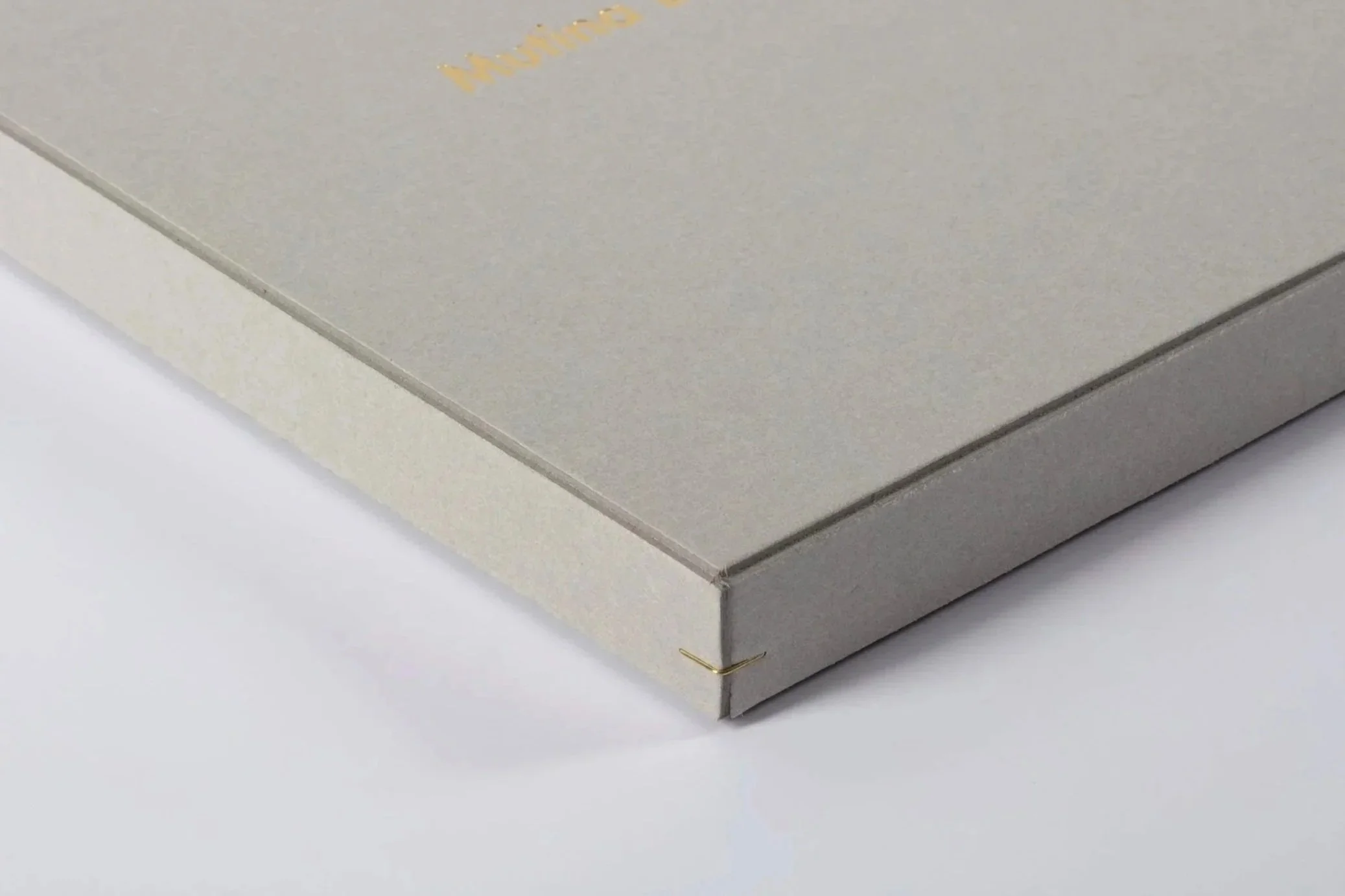 Dettaglio di una scatola di cartone beige con angoli ripiegati, appoggiata su una superficie bianca.