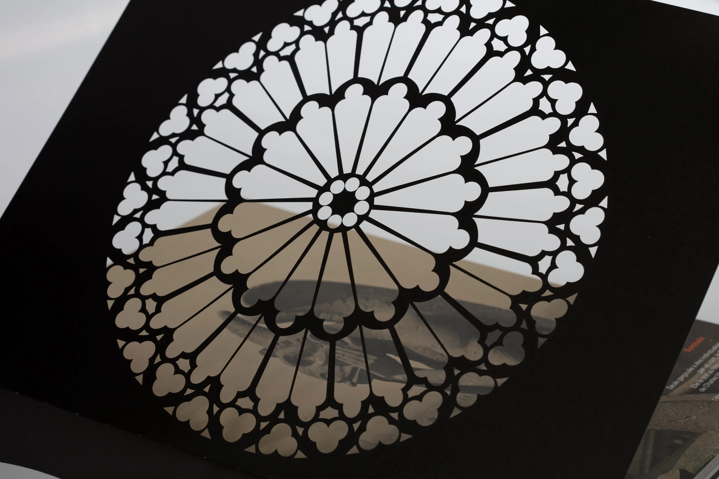 Un vetro decorativo con motivo a rosa dei venti, realizzato con carta tagliata, attraverso il quale si intravede un paesaggio urbano e il mare sullo sfondo.