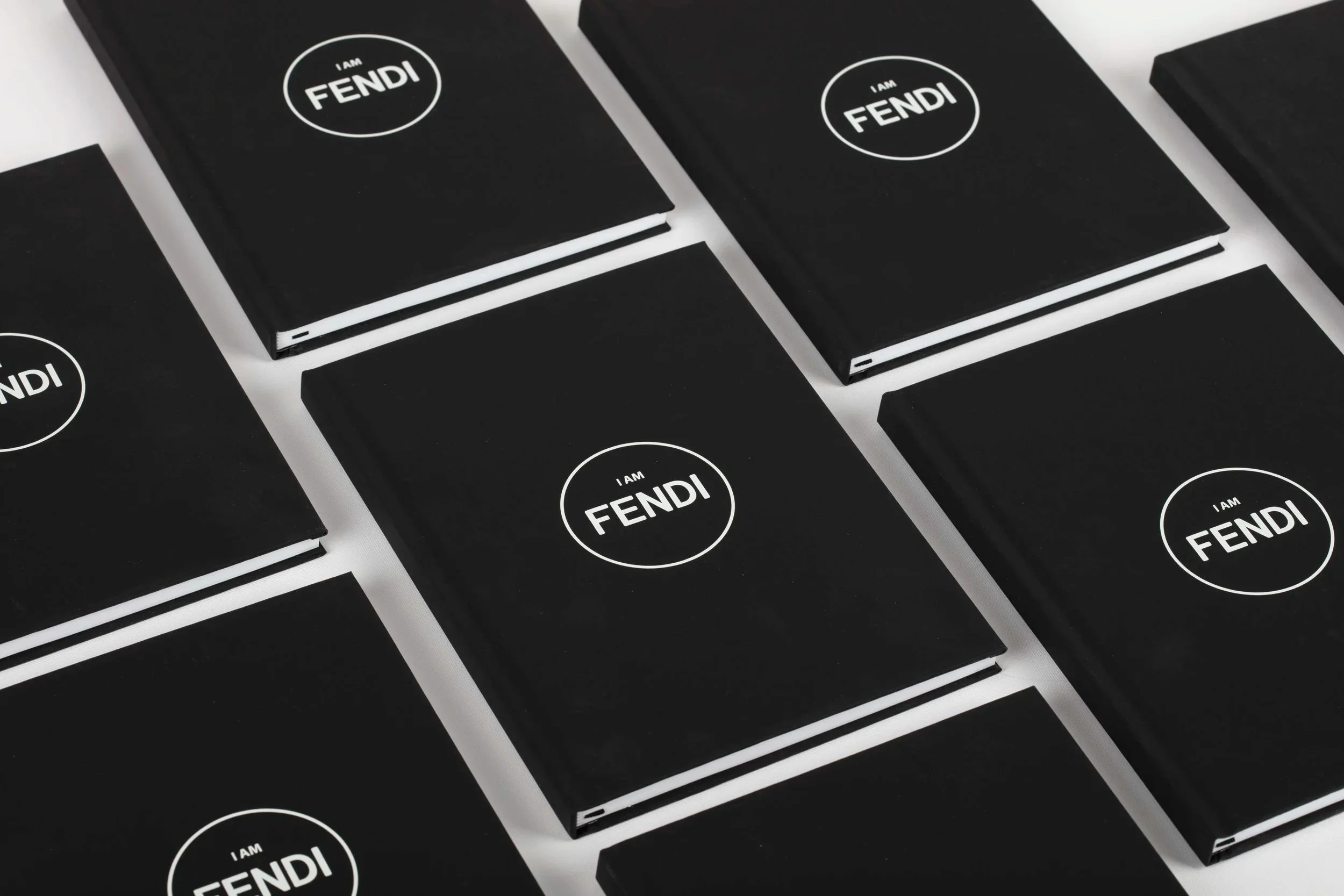 Blocchi di notebook neri con la scritta bianca 'I AM FENDI' disposti in un ordine ordinato su una superficie bianca.