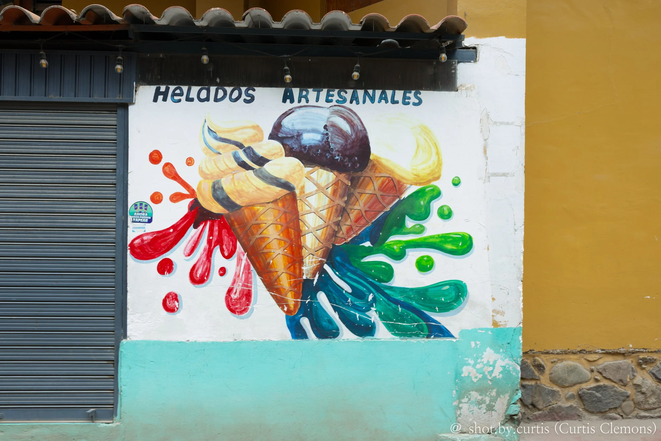 Colorful mural of an ice cream cone with swirling ice cream, painted on a building wall with a yellow and teal background and a stone foundation.
