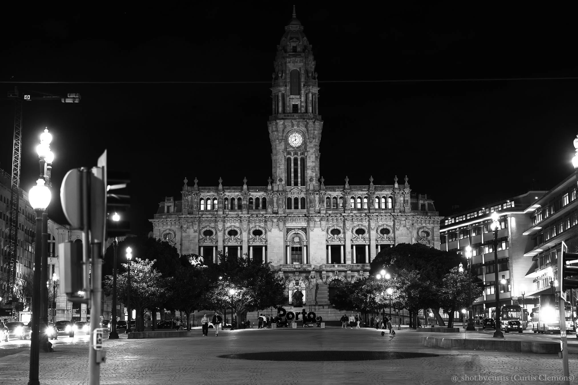 Nighttime view of Porto City Hall in Portugal illuminated against the dark sky, with people walking and cars parked in the foreground.