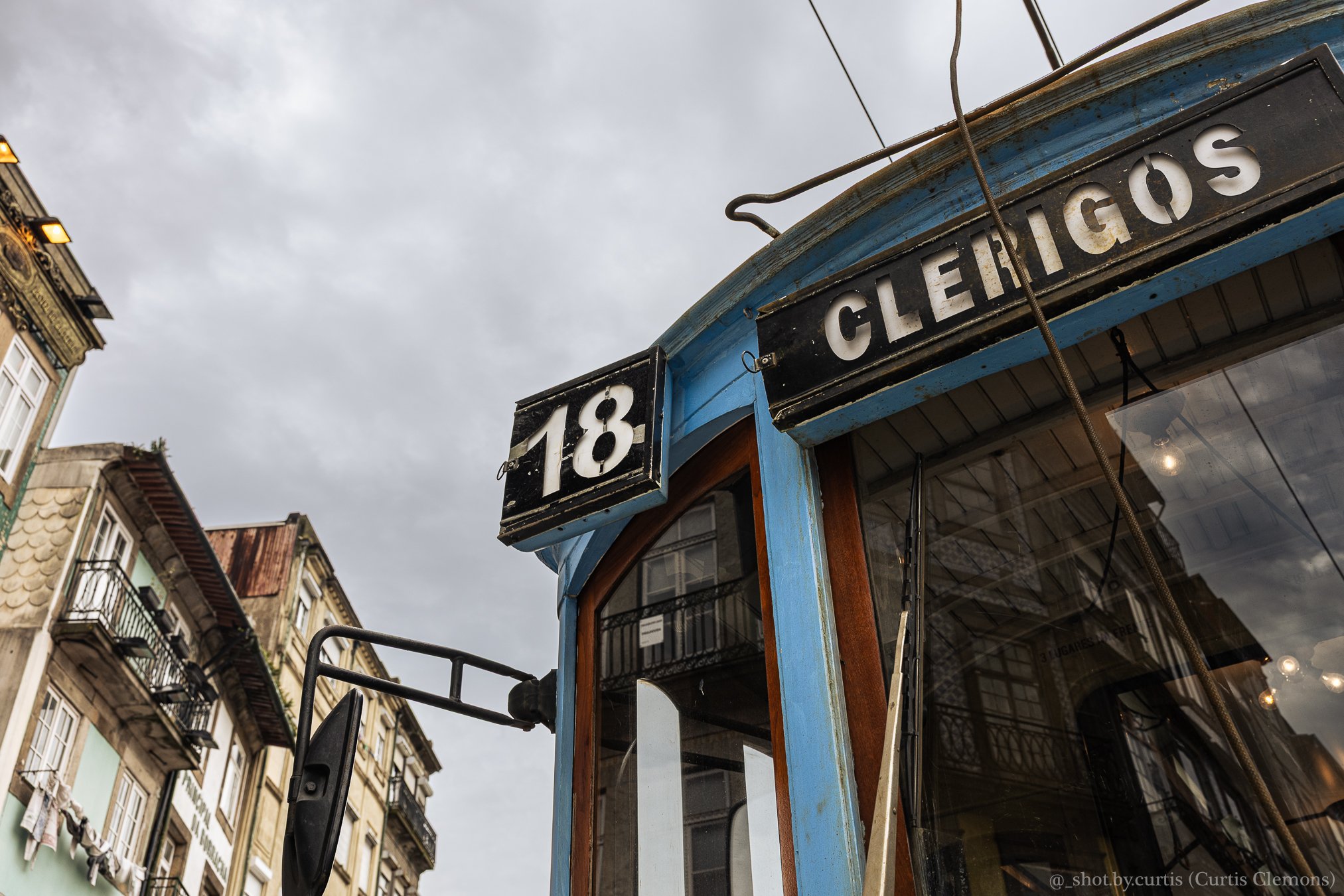 Close-up of a vintage blue trolley with a 'CERRIGOS' sign, set against a backdrop of historic apartment buildings and a cloudy sky.