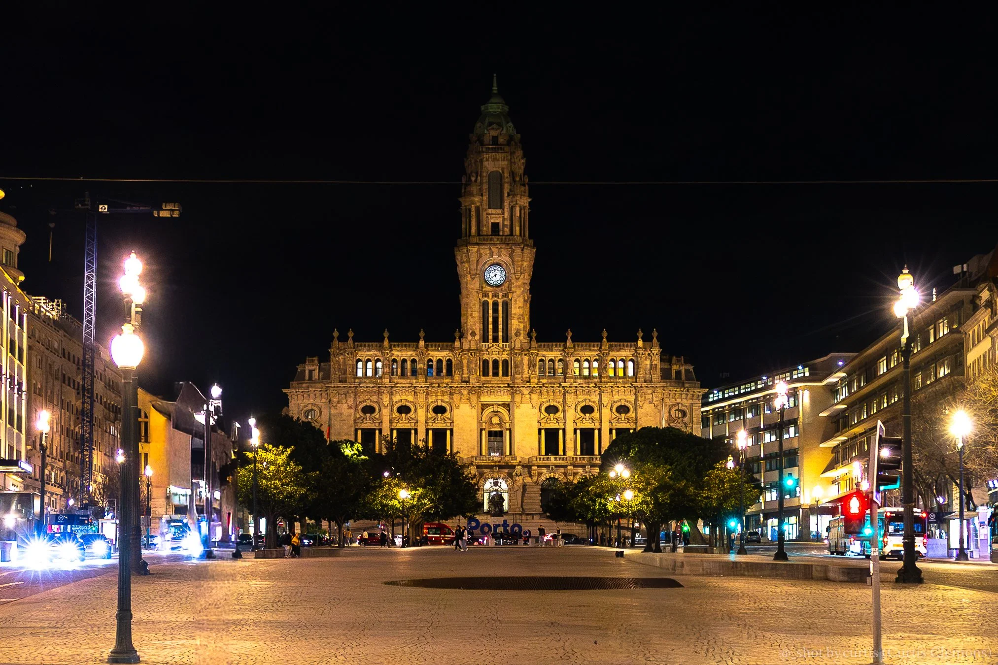 Night view of an ornate historic building with a clock tower, illuminated and surrounded by city street lights and buildings.