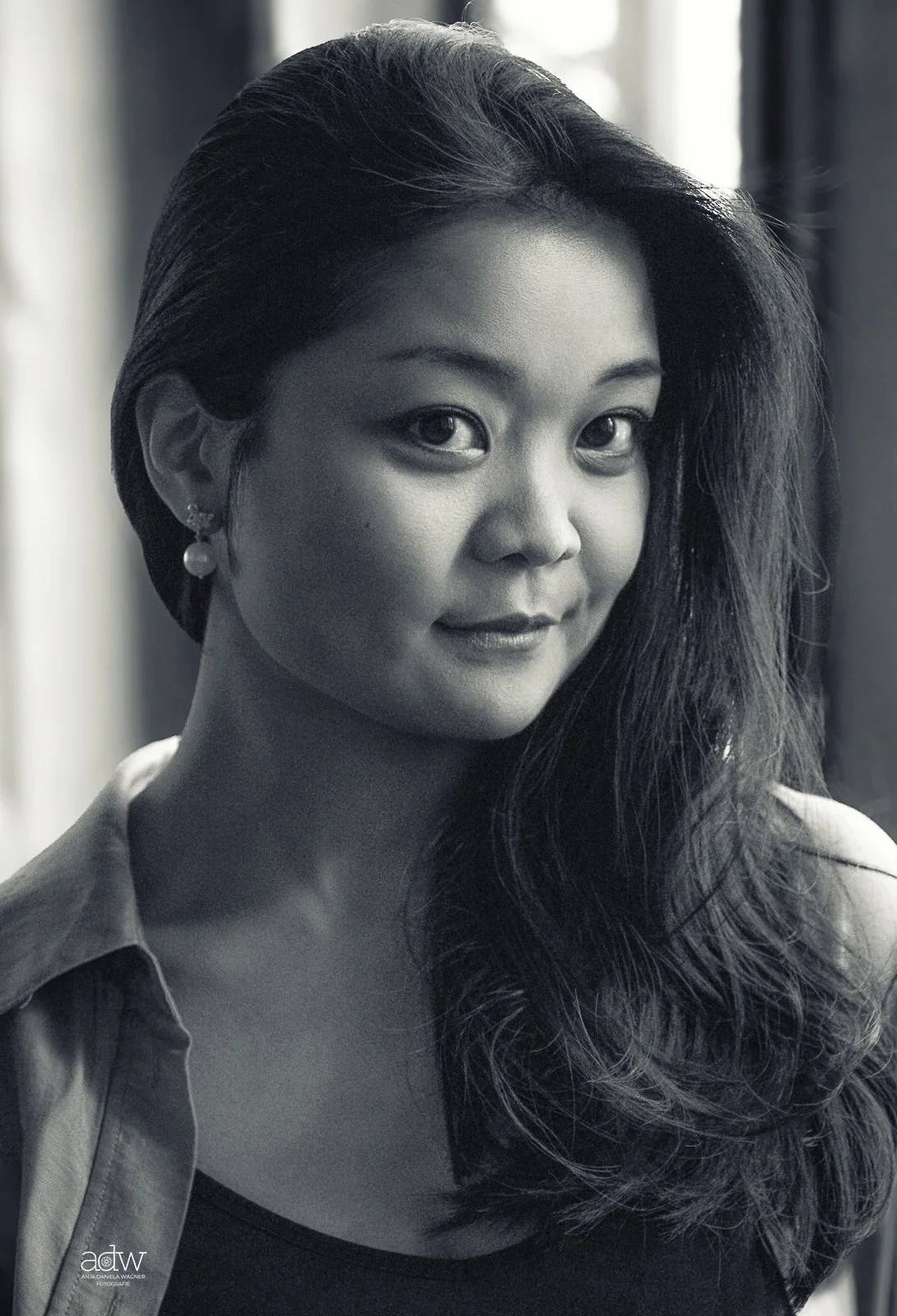 Black and white portrait of a woman with long wavy hair, wearing earrings and a collared shirt, looking at the camera with a slight smile.