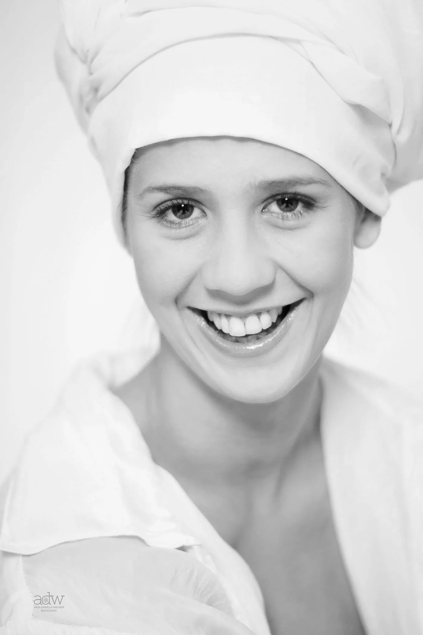 Close-up black-and-white photo of a woman wearing a chef's hat and smiling, with her face filling most of the frame.
