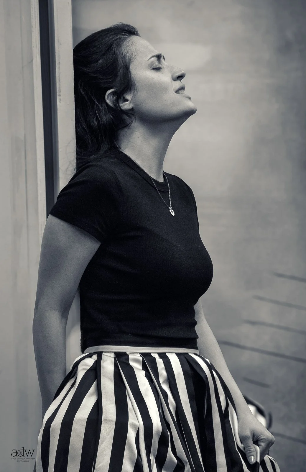 Black and white photo of a woman leaning against a wall with her eyes closed.