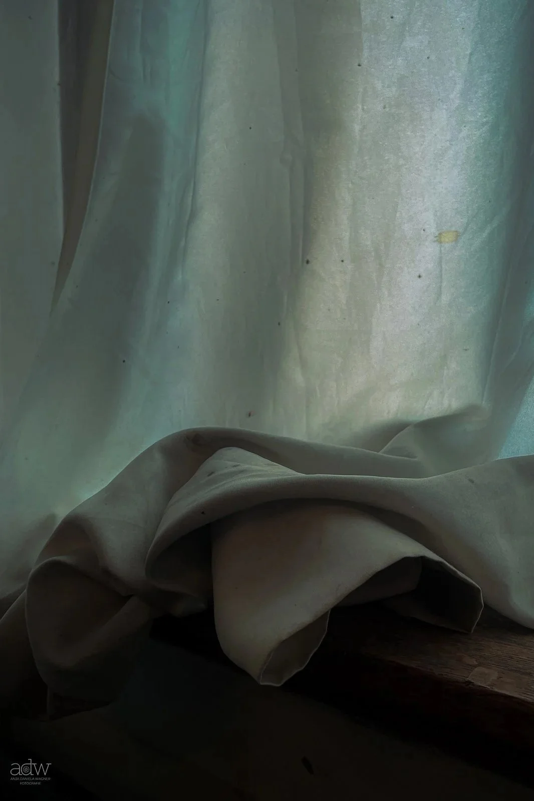 A close-up view of a white curtain with light coming through, and a beige fabric draped over a wooden surface at the bottom of the image.