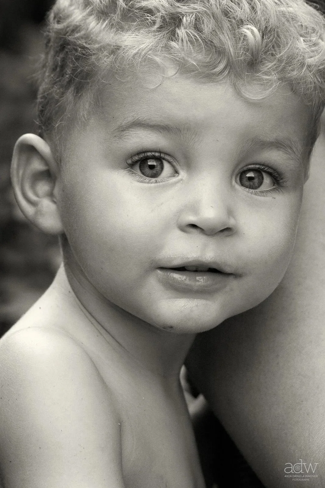 Close-up black and white portrait of a young boy with curly hair, large expressive eyes, and slightly parted lips.