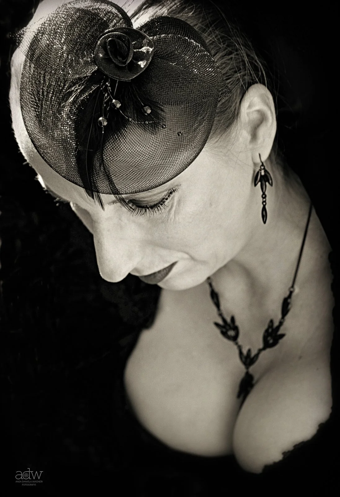 A black and white portrait of a woman with her eyes closed, wearing a decorative headpiece, earrings, and a necklace.