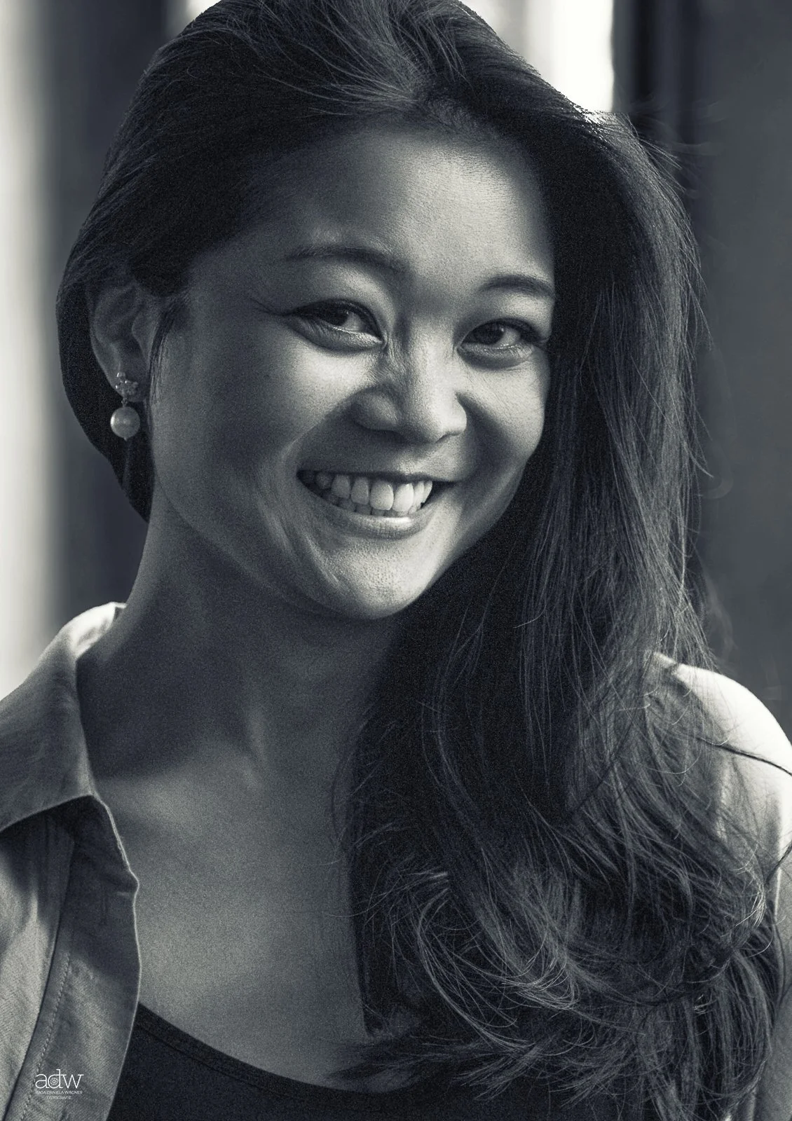 Black and white portrait of a smiling woman with long hair, wearing earrings and a collared shirt.