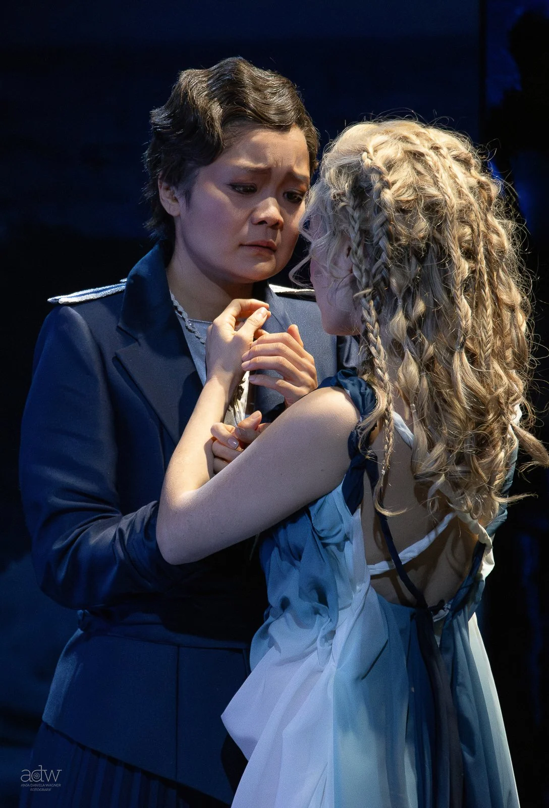 Two women, one in a military uniform and the other in a dress, share an emotional moment, touching foreheads and holding hands, in a dramatic scene.
