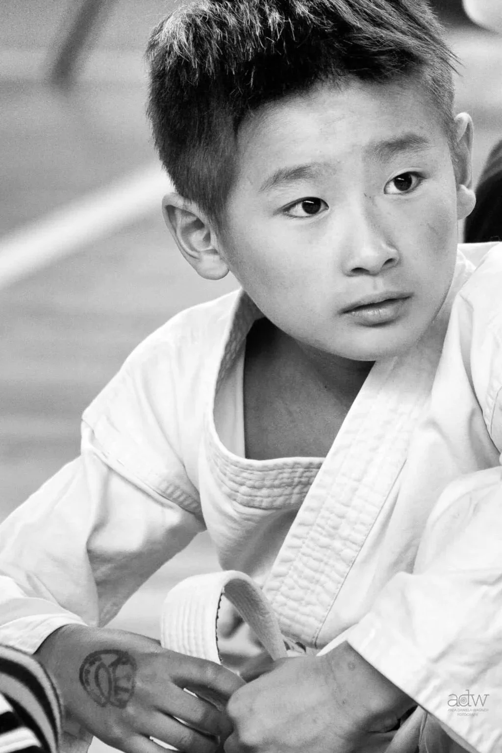 A young boy with short hair in a martial arts gi, looking intently to the side, in black and white.