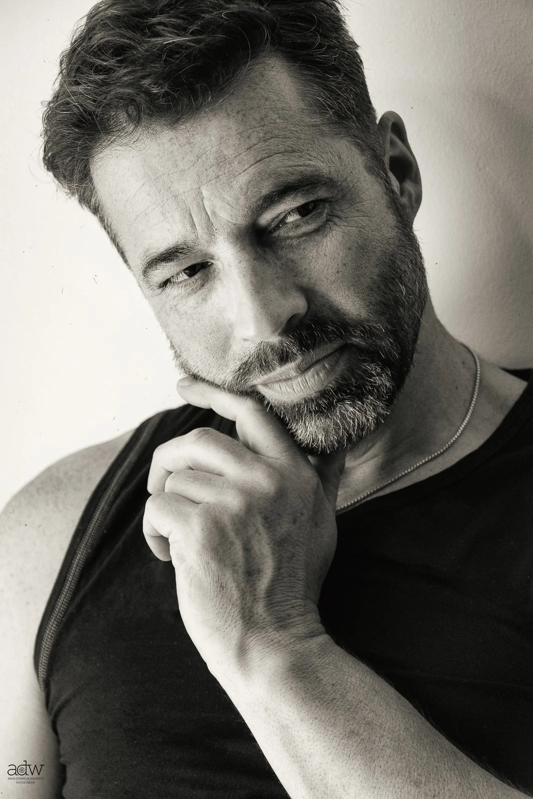 Black and white portrait of a man with a beard, short hair, and a thoughtful expression, touching his chin with his hand.