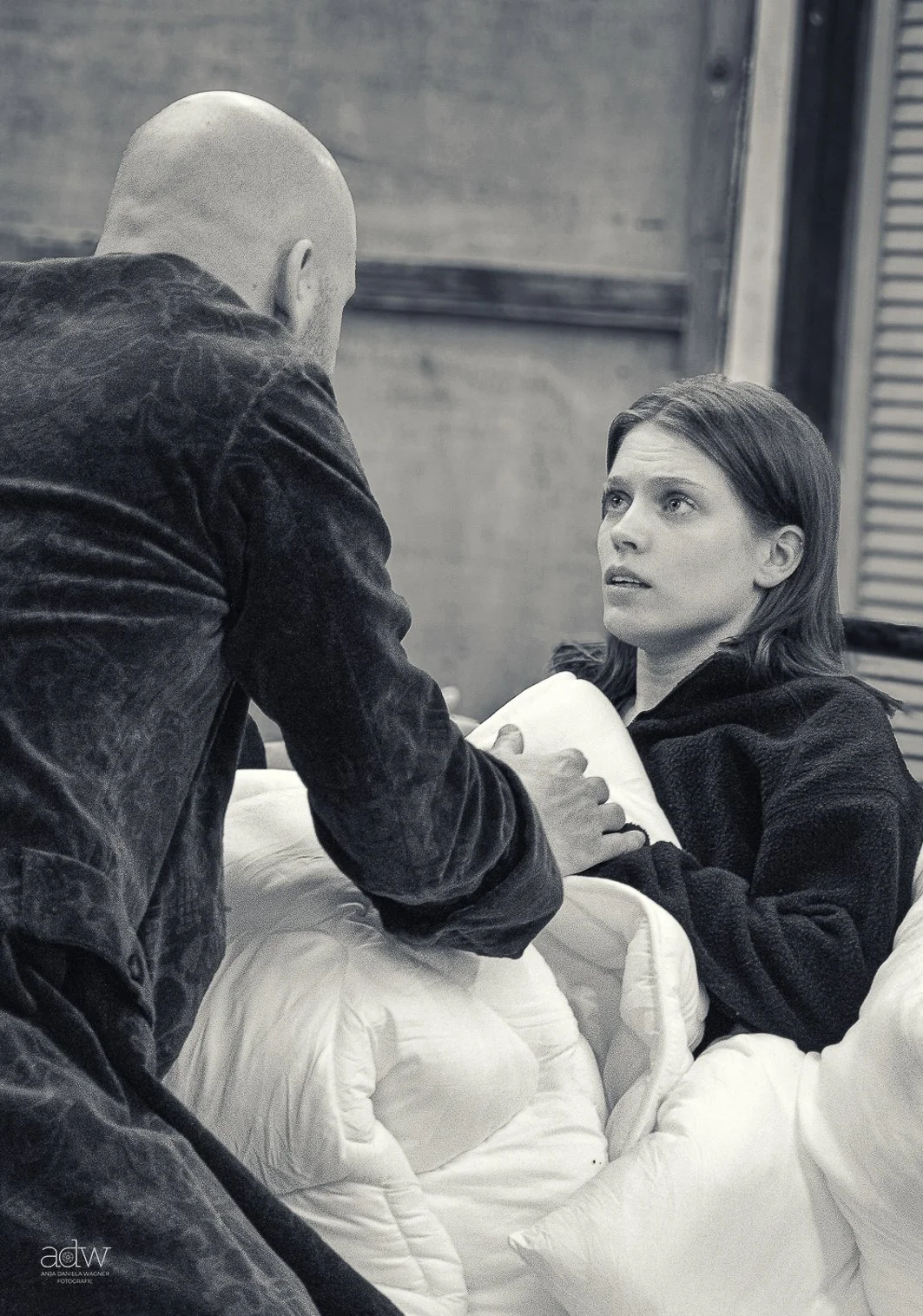 A woman lying in a hospital bed, looking up at a man standing beside her, who appears to be a medical professional holding her hand, in a black and white photo.
