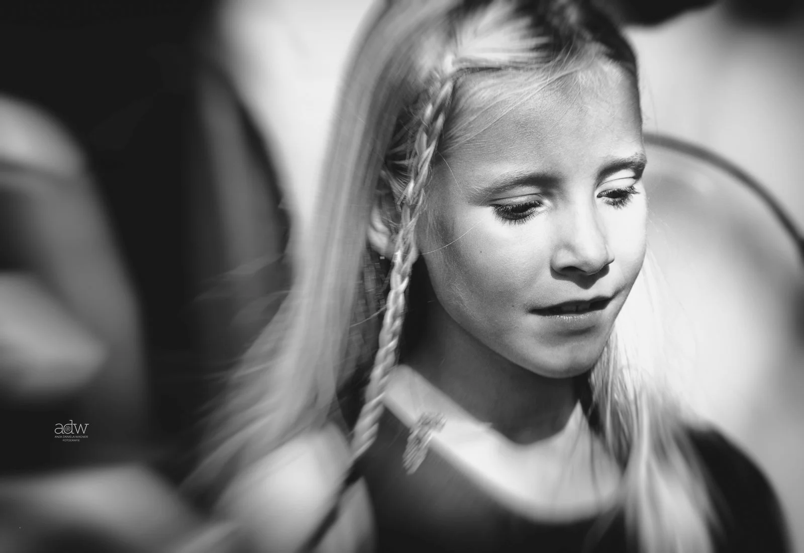 Black and white photo of a young girl with braided hair, looking down, with a blurred background.