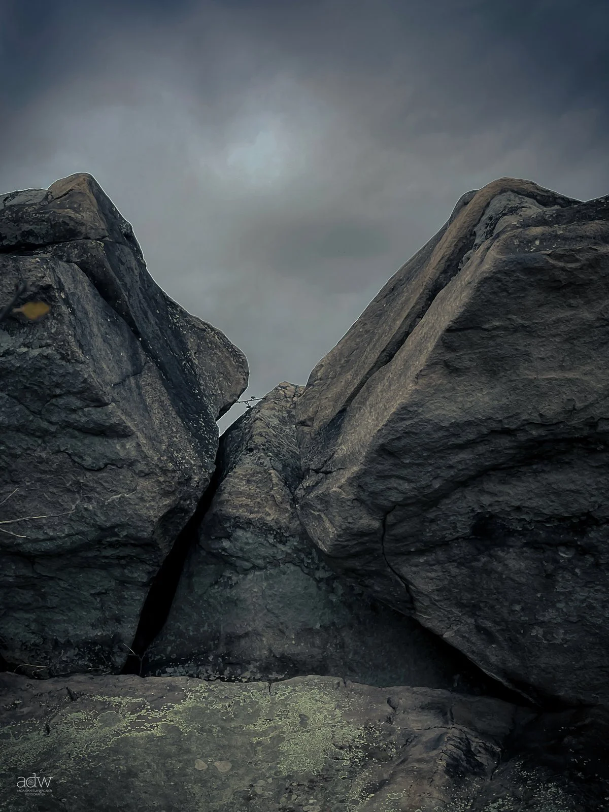 Large dark gray rocks with a narrow crevice between them, under a cloudy, overcast sky.