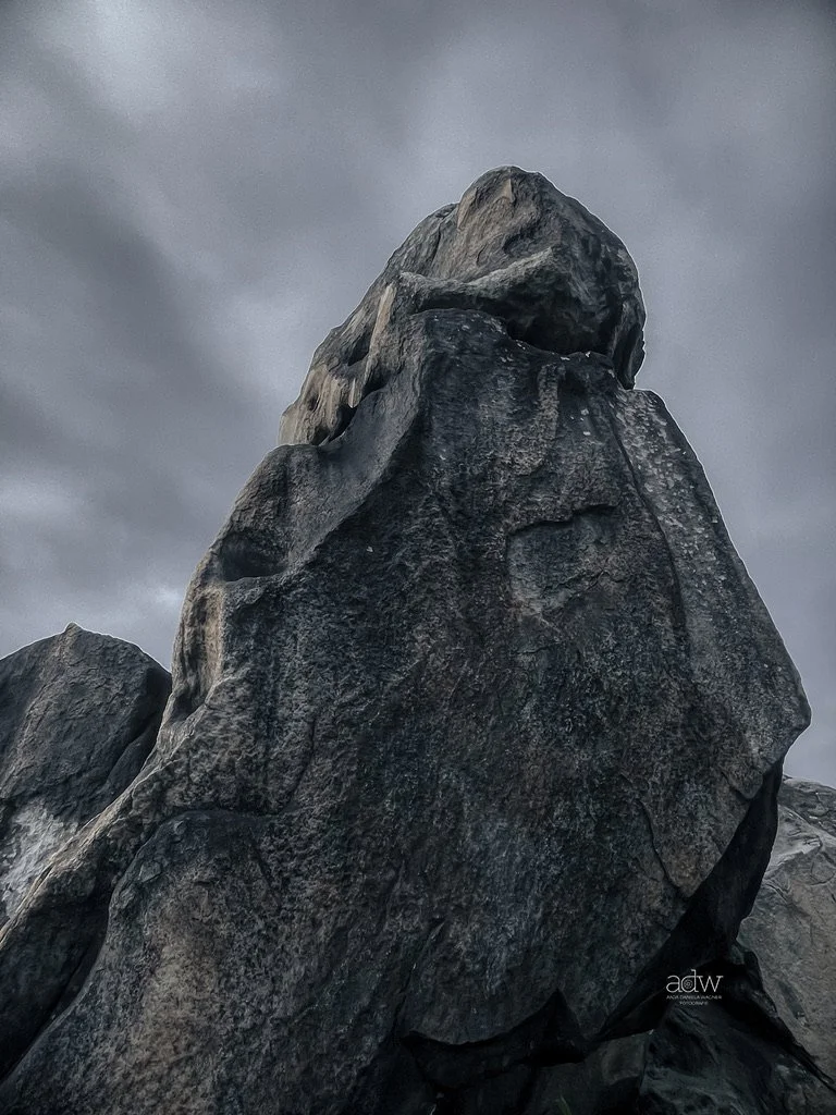 Large dark gray rock formation with an overhanging section against a cloudy, overcast sky.