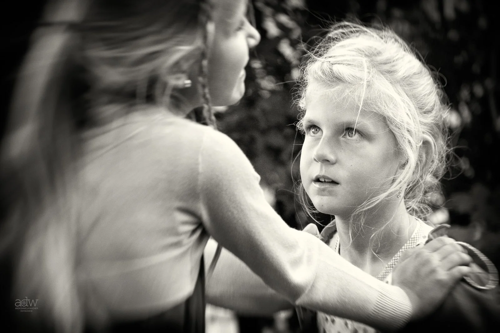 Black and white photo of a woman with long hair looking at a young girl with curly hair and light eyes, who is gazing up at her.