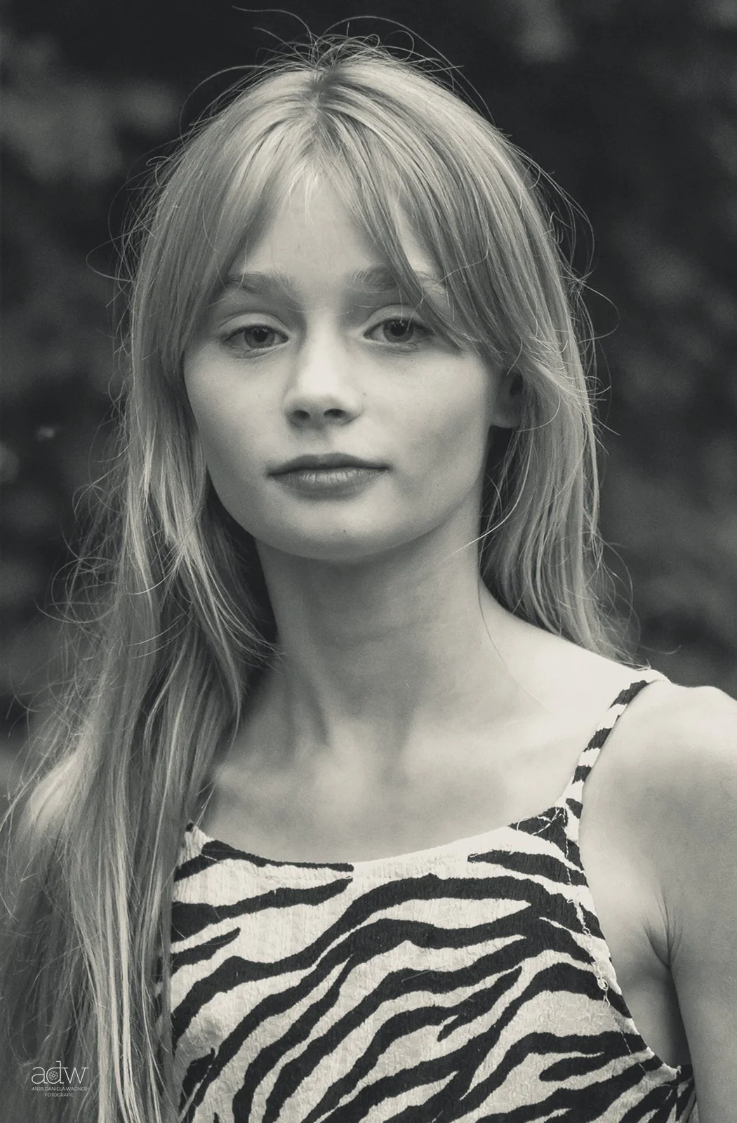 Black and white portrait of a young woman with long hair, wearing a zebra print top, gazing at the camera with a calm expression.