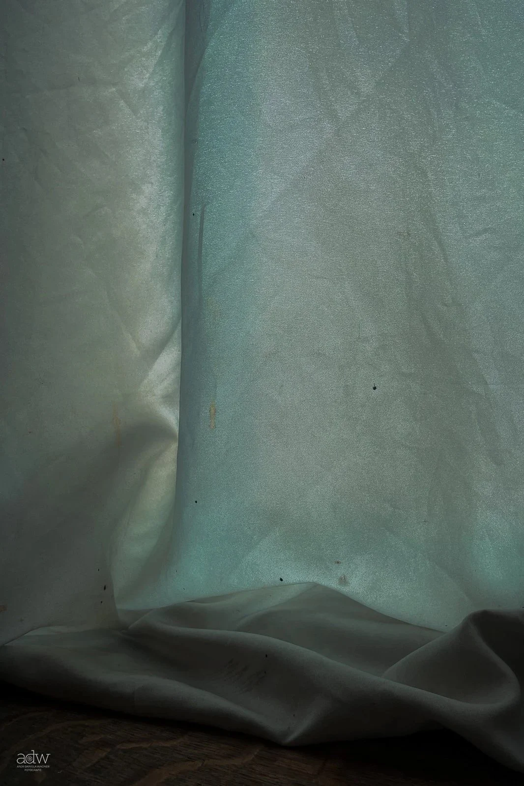 Inside view of a light-colored, slightly wrinkled fabric or paper material with some small dark spots and a subtle seam or fold line, illuminated with soft, diffused lighting.