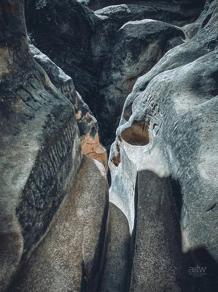 A narrow canyon passage with smooth, weathered rock walls, eroded into unique shapes and formations.