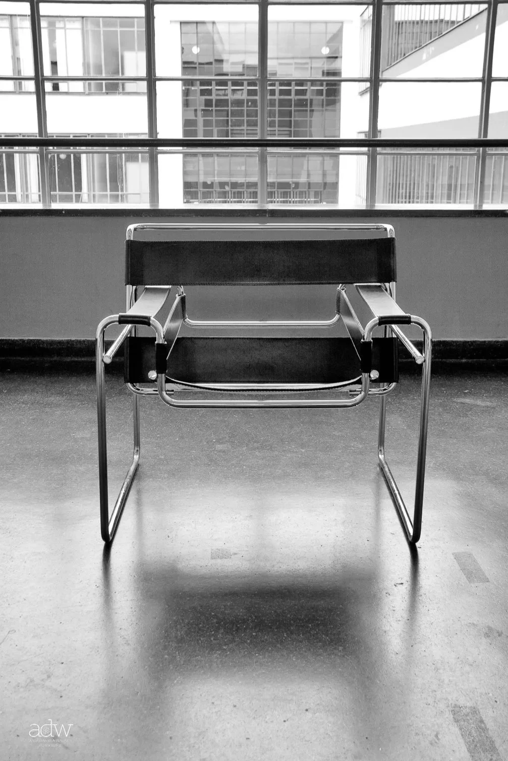 Empty modern waiting area with a black chair in front of large window showing office buildings outside.