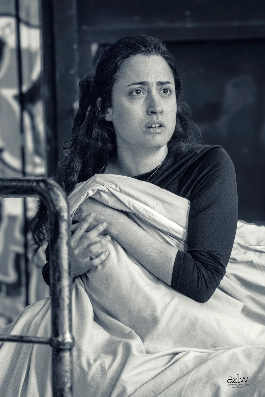 A woman with long dark hair holding a blanket close to her chest, appearing distressed or worried, in a black-and-white photo.