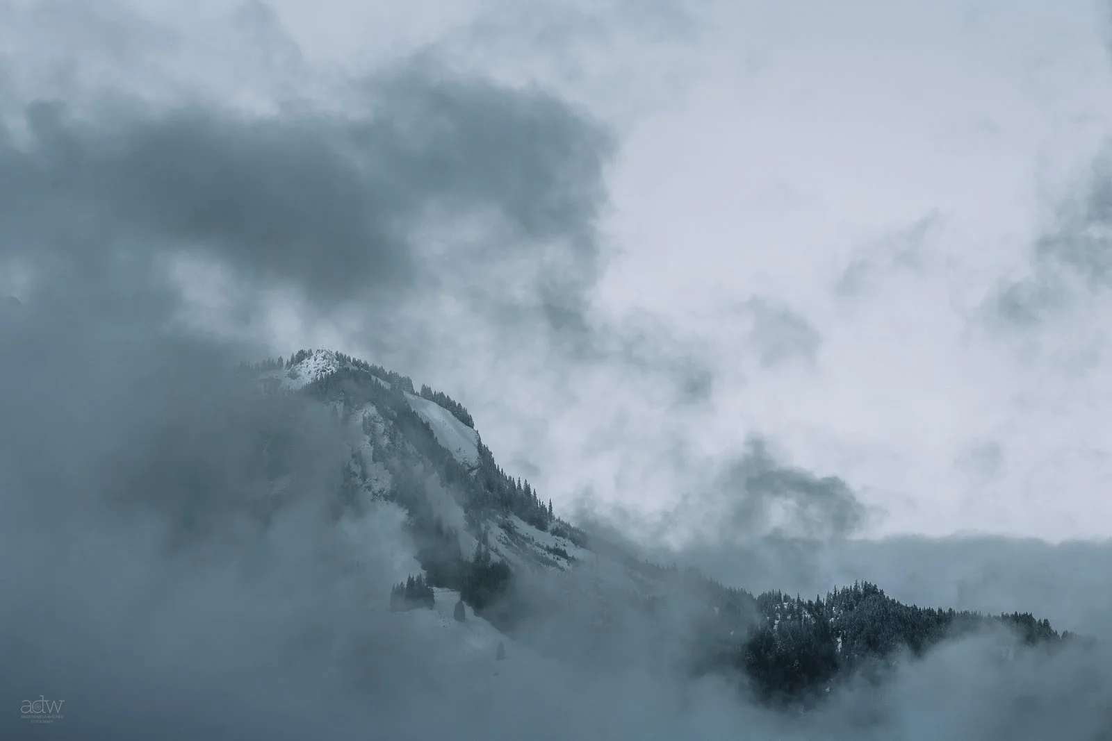Snow-covered mountain partially obscured by clouds.