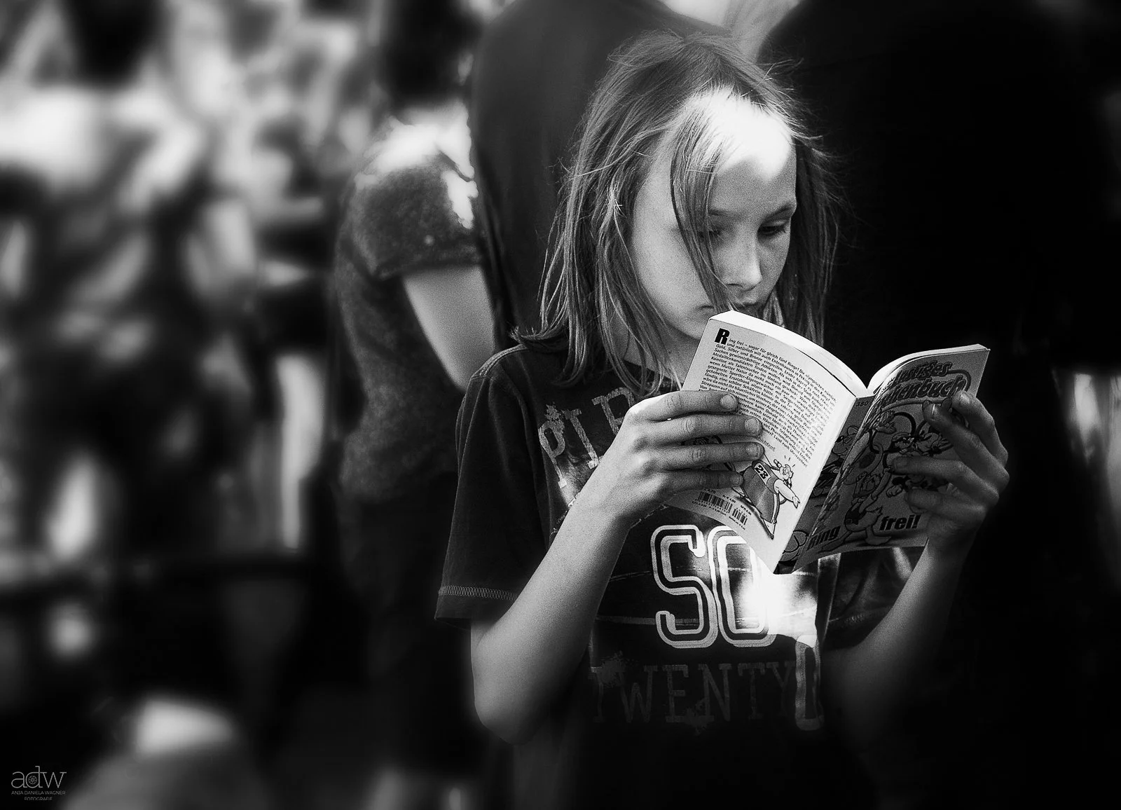 A young girl with long hair reading a comic book in a crowded environment, black and white photograph