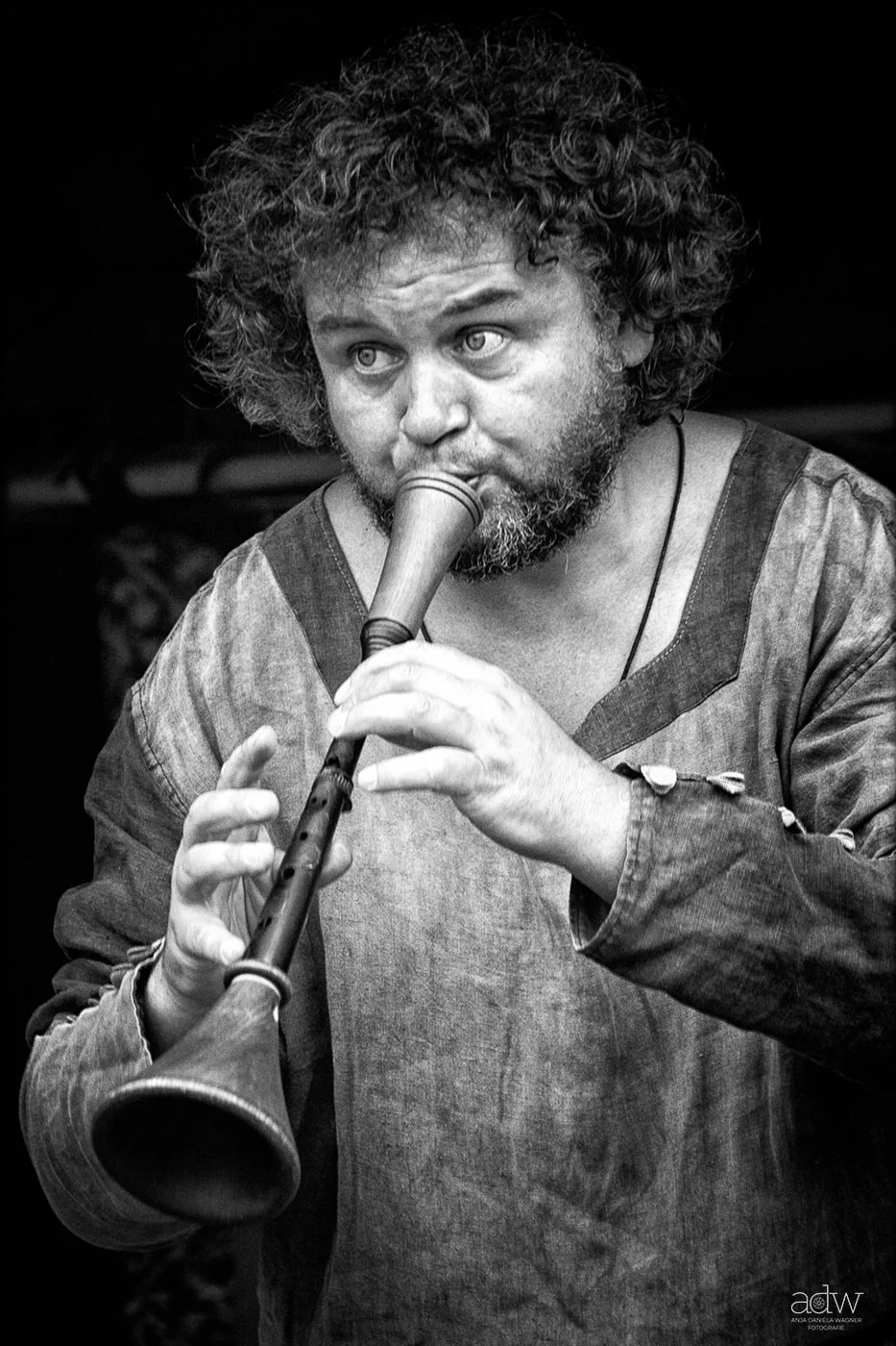 Black and white photo of a man with curly hair and beard playing a recorder flute.