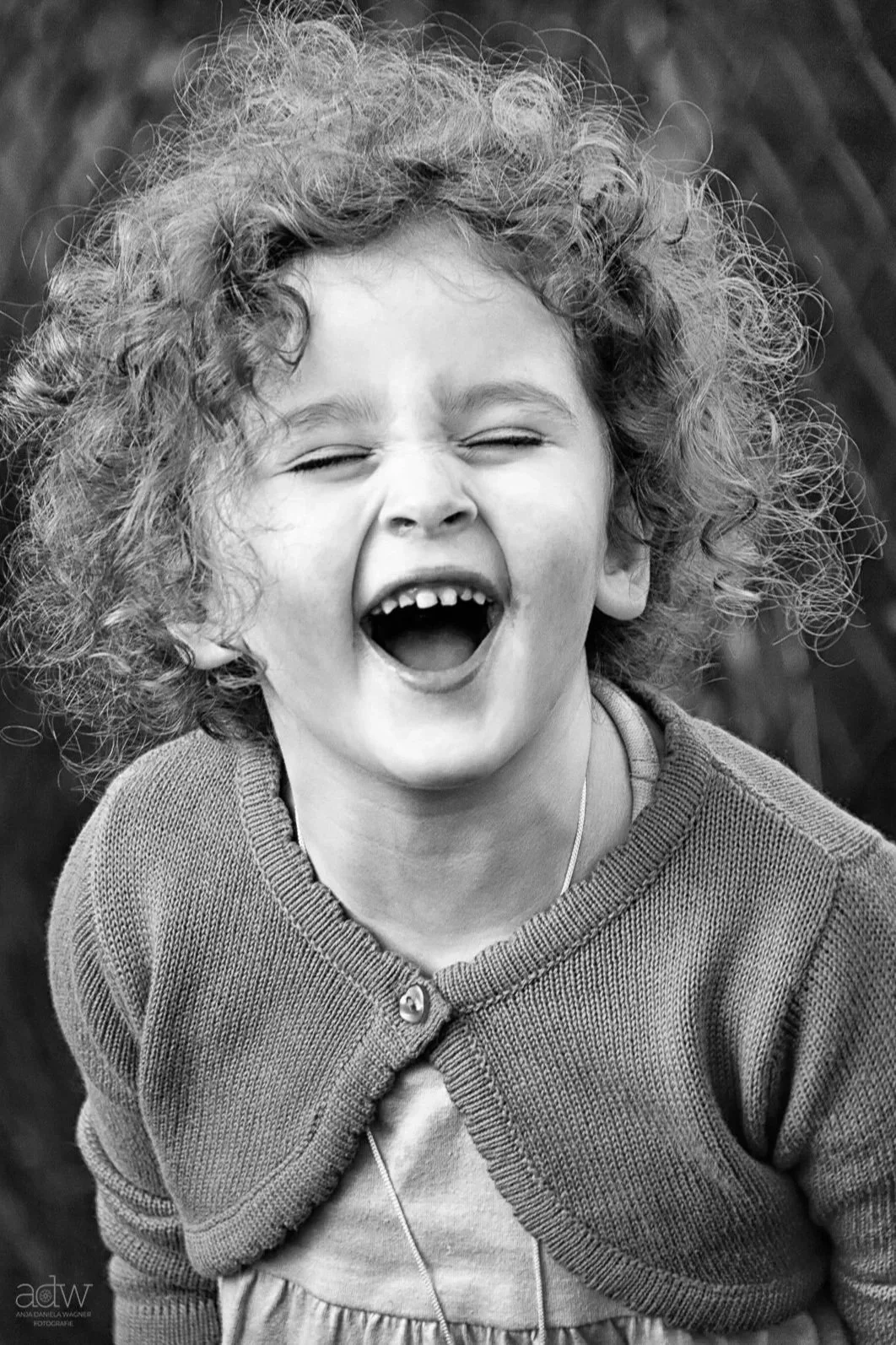 A young girl with curly hair laughing with her mouth open wide, showing her teeth.
