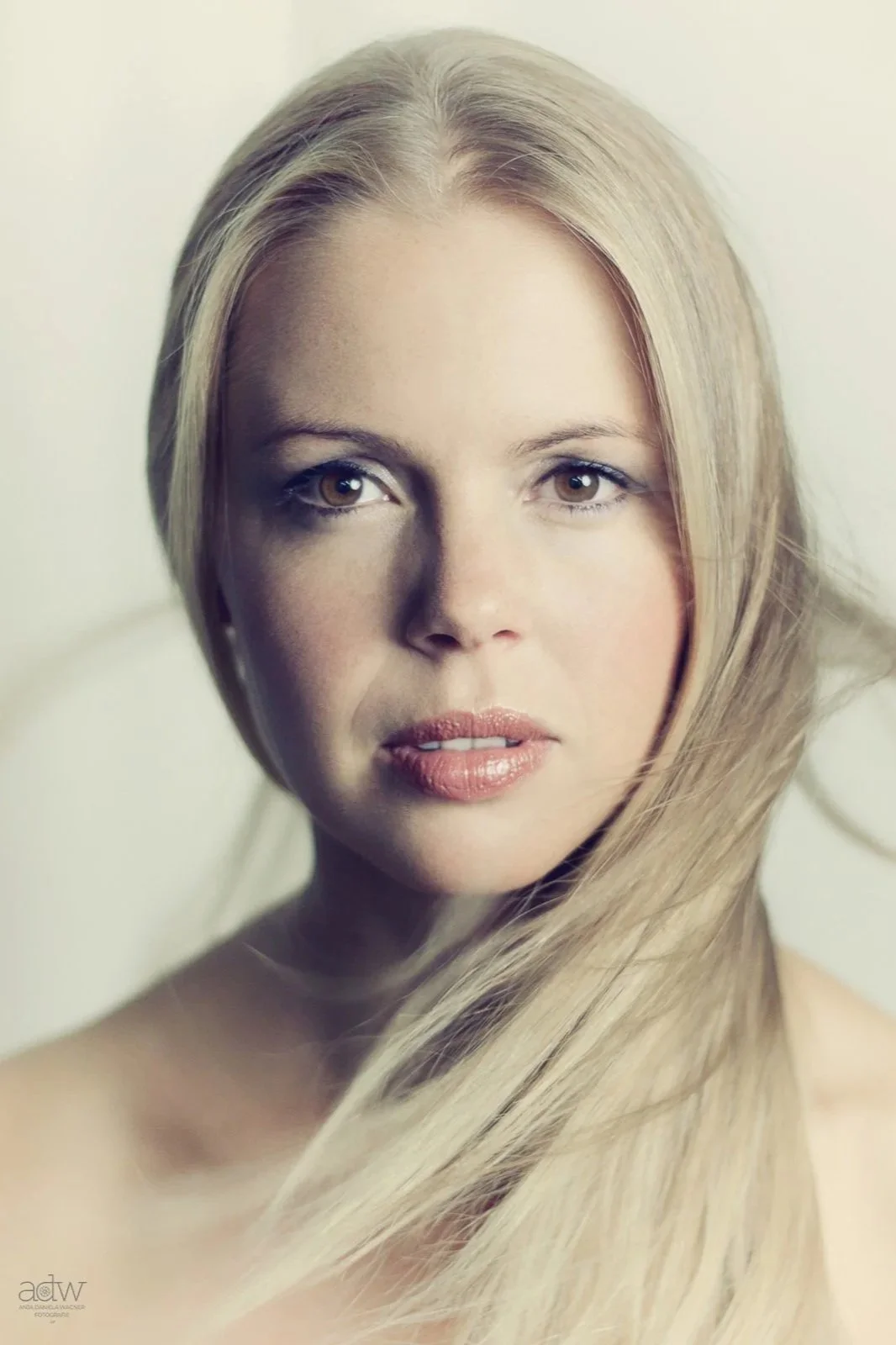 Close-up portrait of a woman with long blonde hair and light skin, looking directly at the camera.