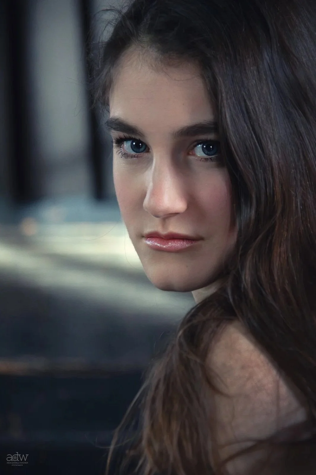 Close-up of a woman with blue eyes and long dark hair, looking at the camera with a serious expression.