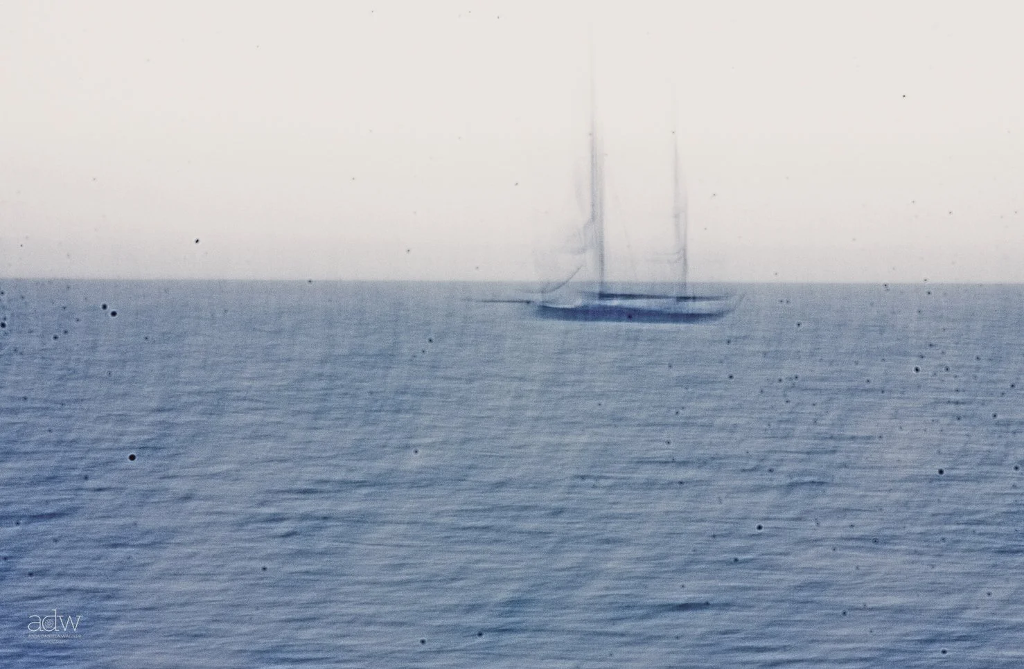 A faint, blurry sailboat on the horizon over a calm ocean, with a mostly overcast sky.