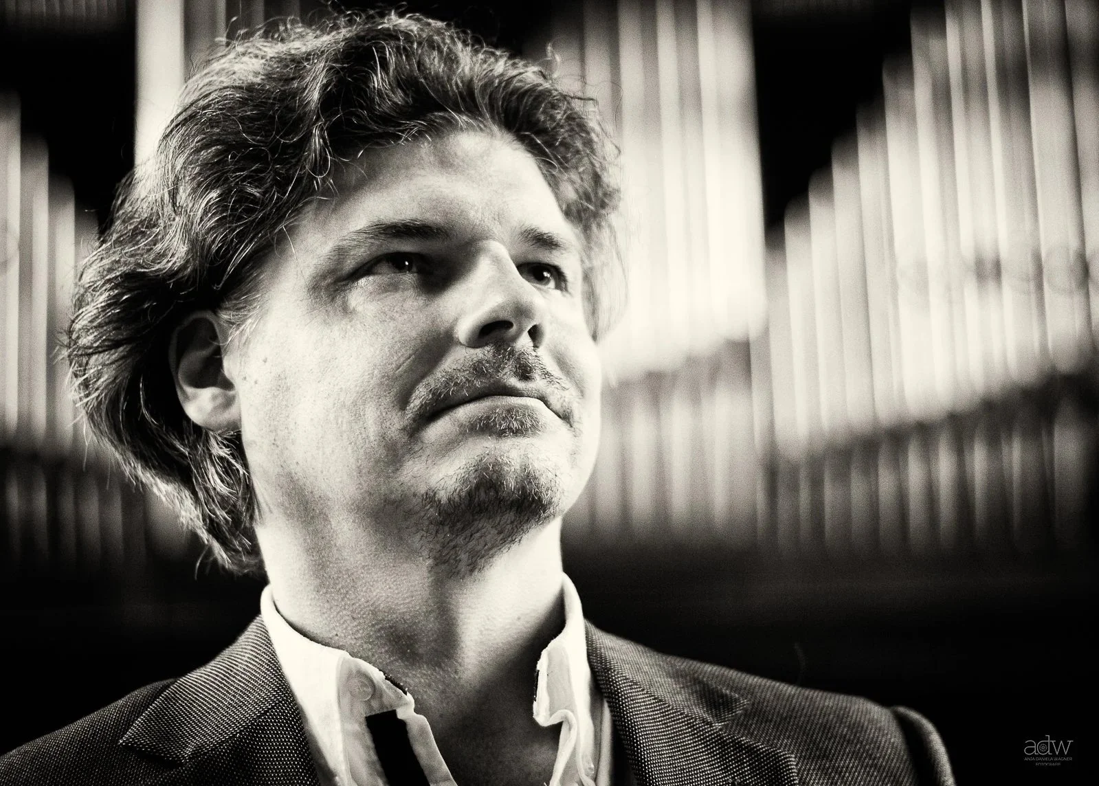 Black and white portrait of a man with curly hair and a mustache, wearing a suit and a white shirt, in front of a bookshelf.