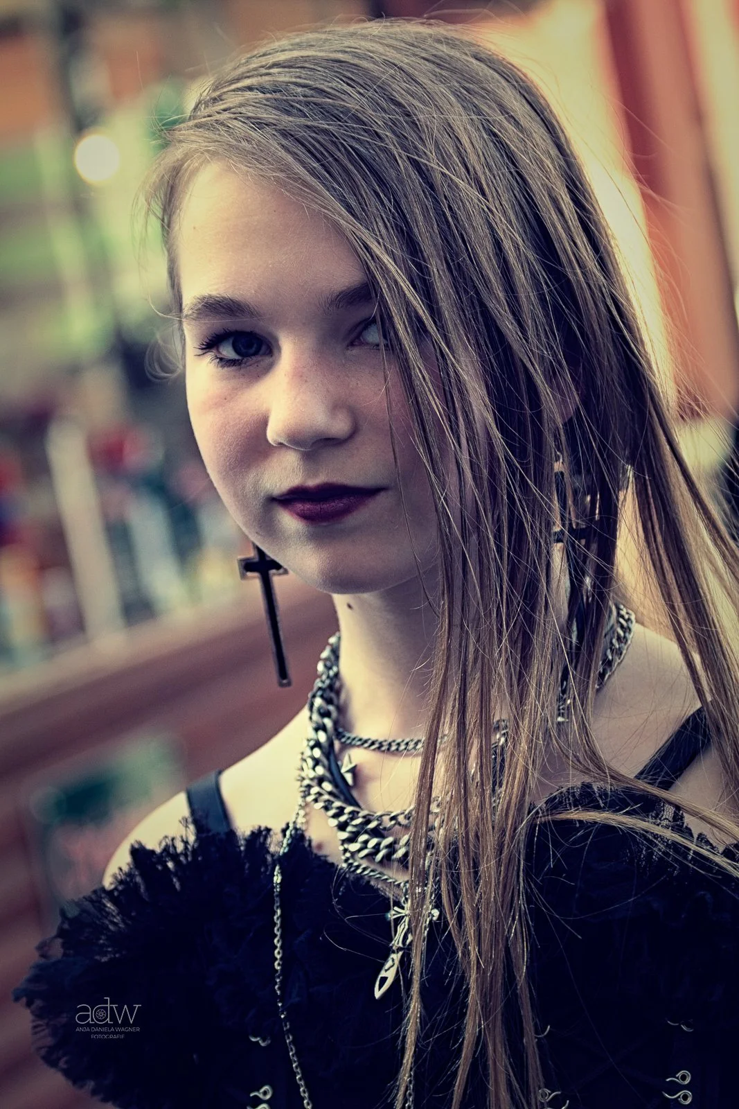 Close-up photo of young woman with long, wet hair, dark lipstick, and gothic-style jewelry, standing outdoors.