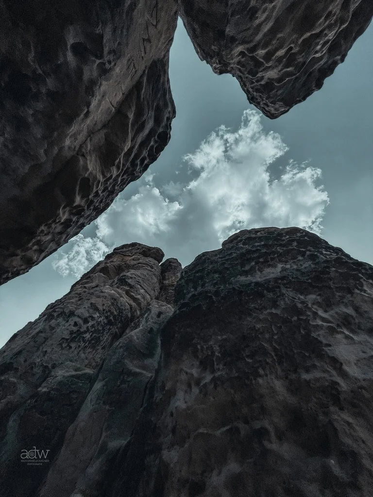 Looking up at large, dark rock formations with a cloudy sky visible through the gap.