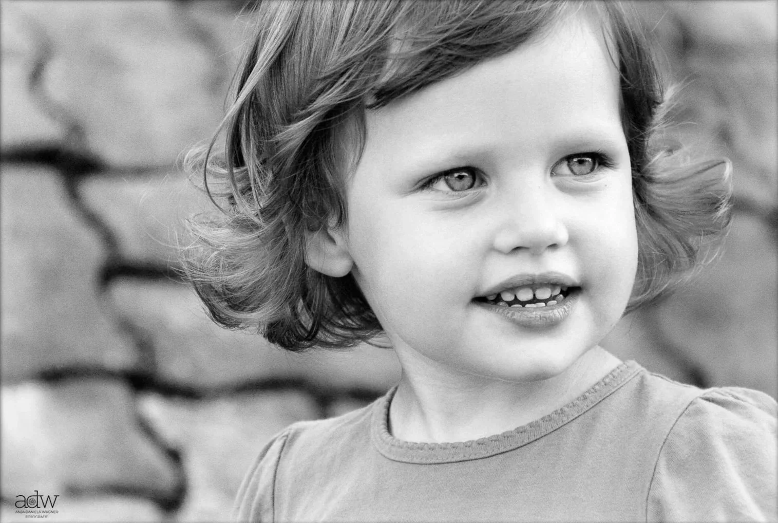 A black and white photo of a young girl with curly hair, looking to the side with a slight smile.