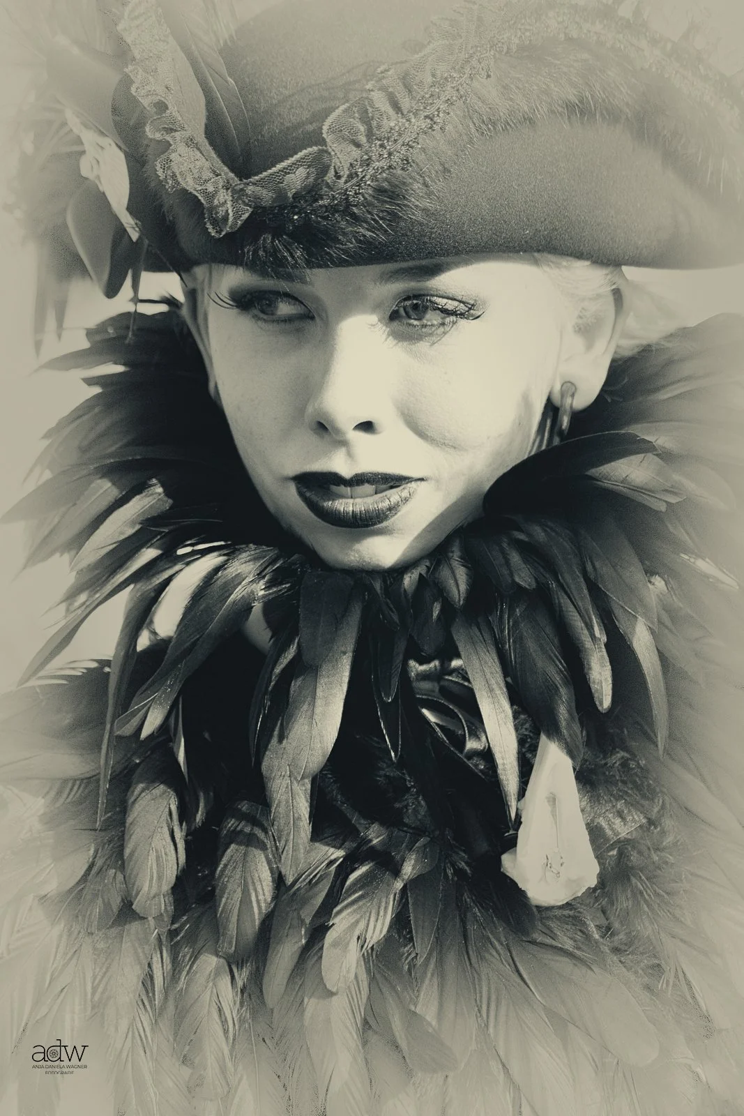 A woman dressed in a costume with a feathered collar and a large feathered hat, looking to the side in a black-and-white photograph.