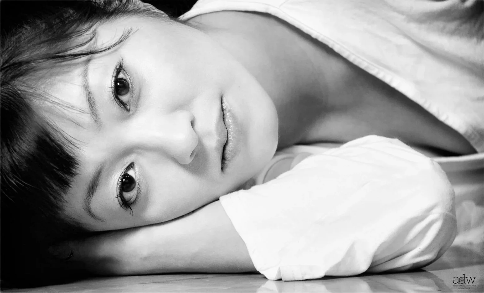 Black and white portrait of a woman lying down, resting her head on her arm, looking at the camera with a gentle expression.