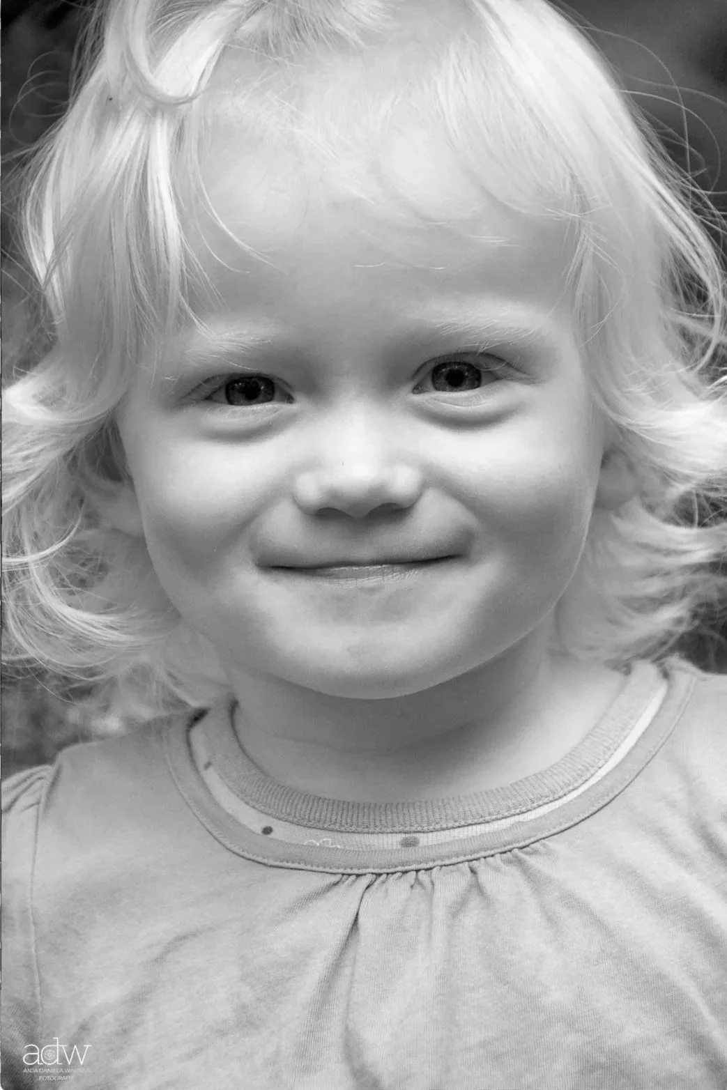 A smiling young girl with curly blonde hair in a portrait photograph.